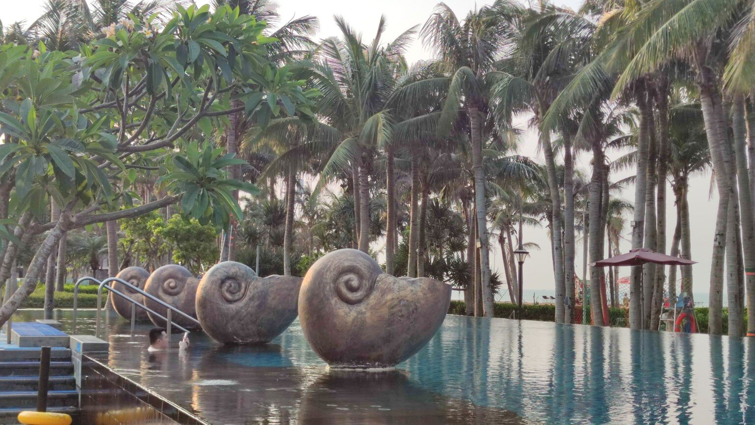 Schwimmbecken mit großen Schneckenfiguren und Palmen in Haikou