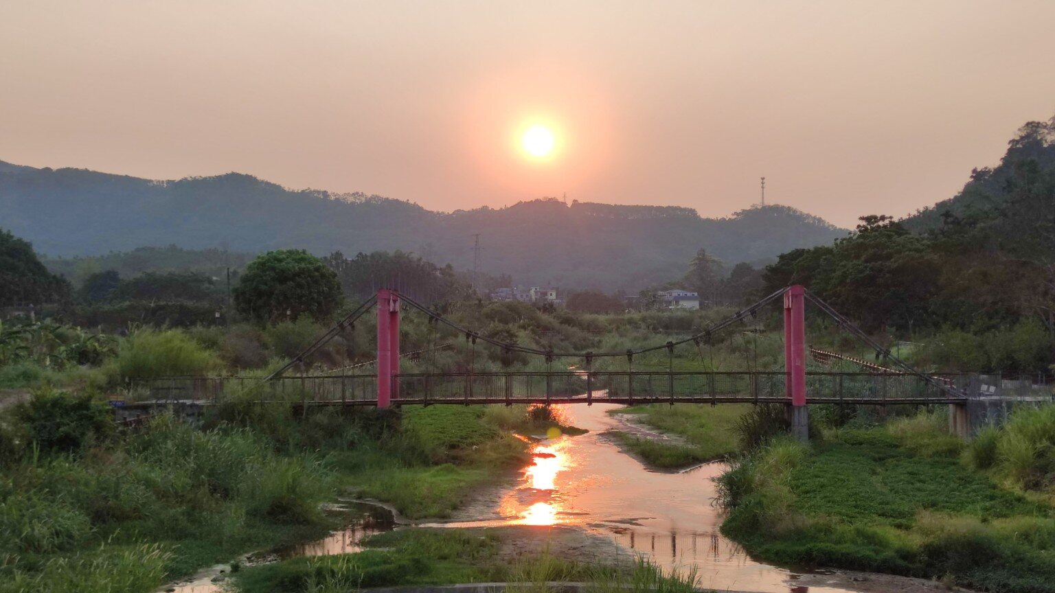Sonnenuntergang über einem Fluss und einer Hängebrücke in Qiongzhong