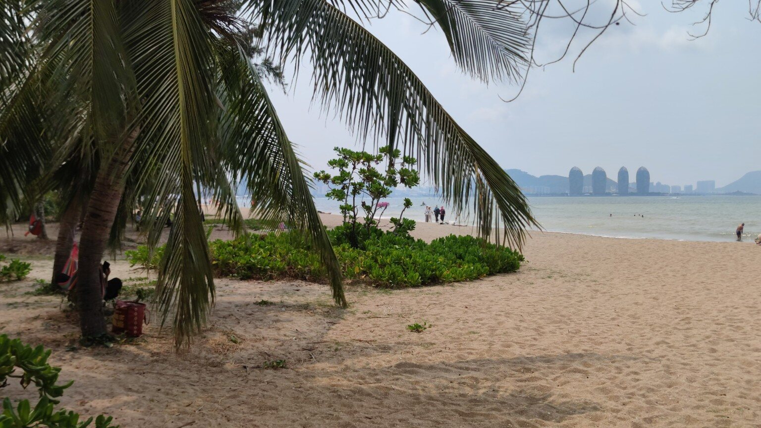 Sandstrand mit Kokospalmen und Blick auf die Küste von Sanya